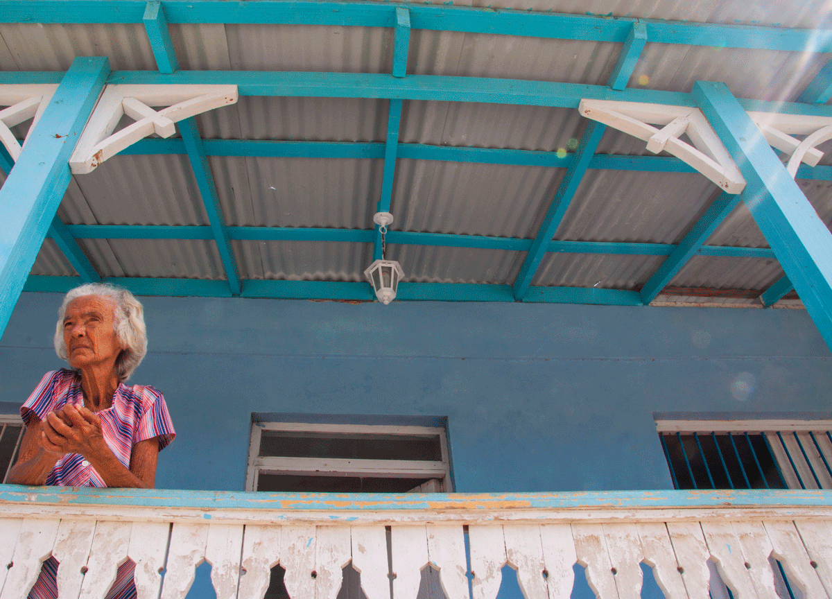 Older woman standing on a balcony looking out over the ledge.